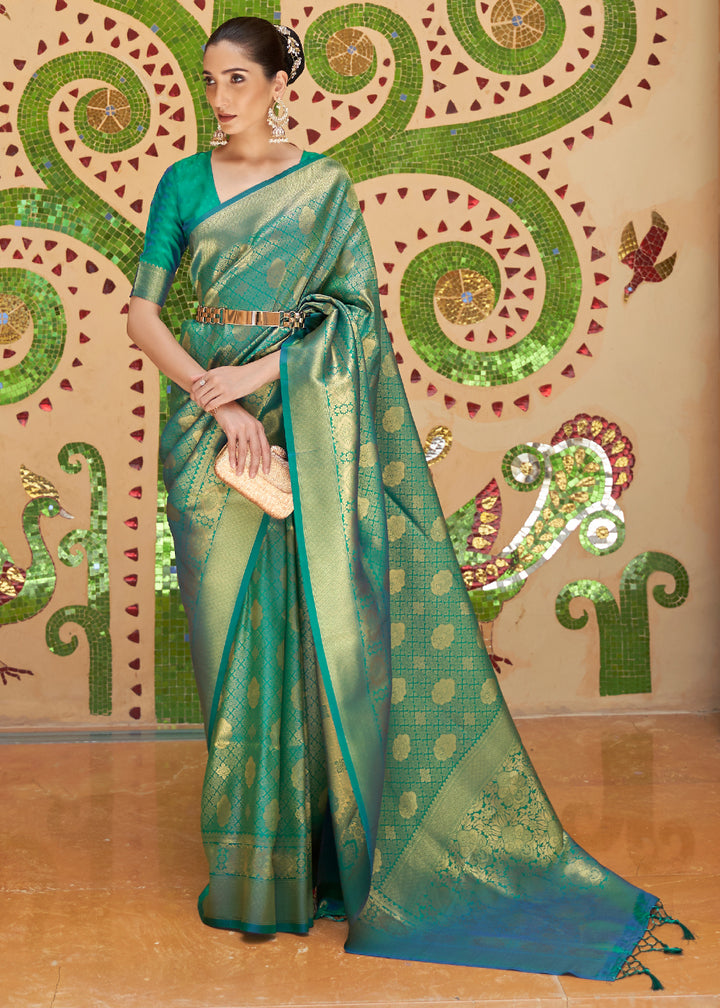 A woman showcasing a green Kanjivaram silk saree with zari woven butti, along with a blue blouse piece, against a decorative background.