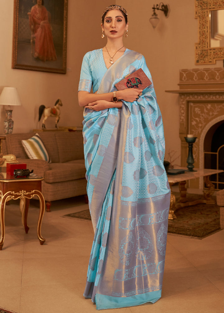 A woman showcasing a sky blue Kanjivaram silk saree with copper zari work, standing in a room with classical decor.